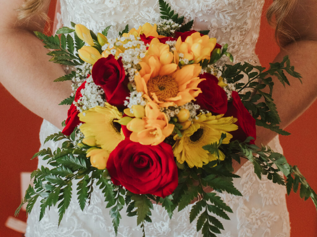 Bride holding a bouquet of ferns, red roses, sunflowers and baby's breath.