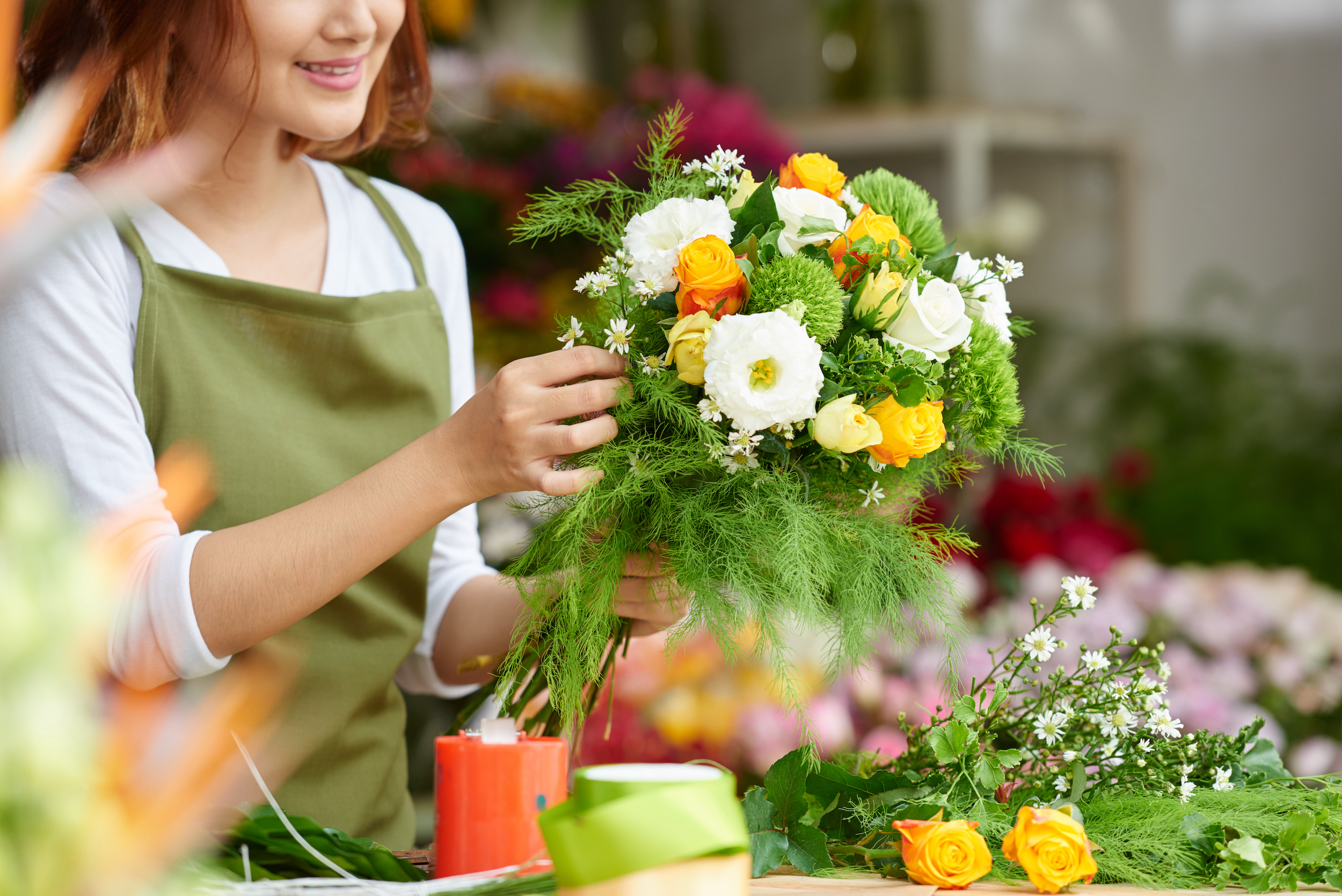 A woman making a bouquet with ferns and white and orange flowers. She is using bulk greenery to arrange the bouquet. 
