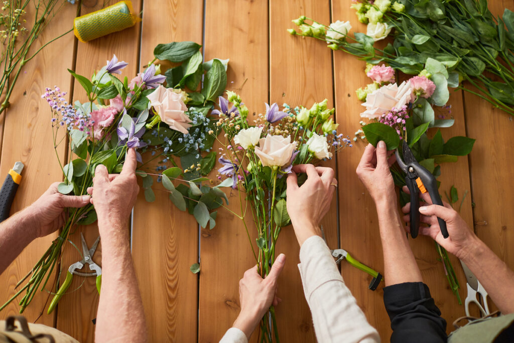 3 sets of hands arranging bouquets with floral foliage and flowers.