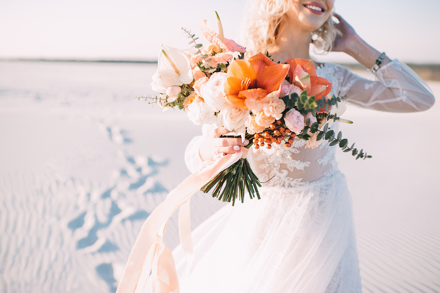 Photo of a bride holding a tropical bouquet made with anthurium, roses, carnations, eucalyptus in white-peach shades.