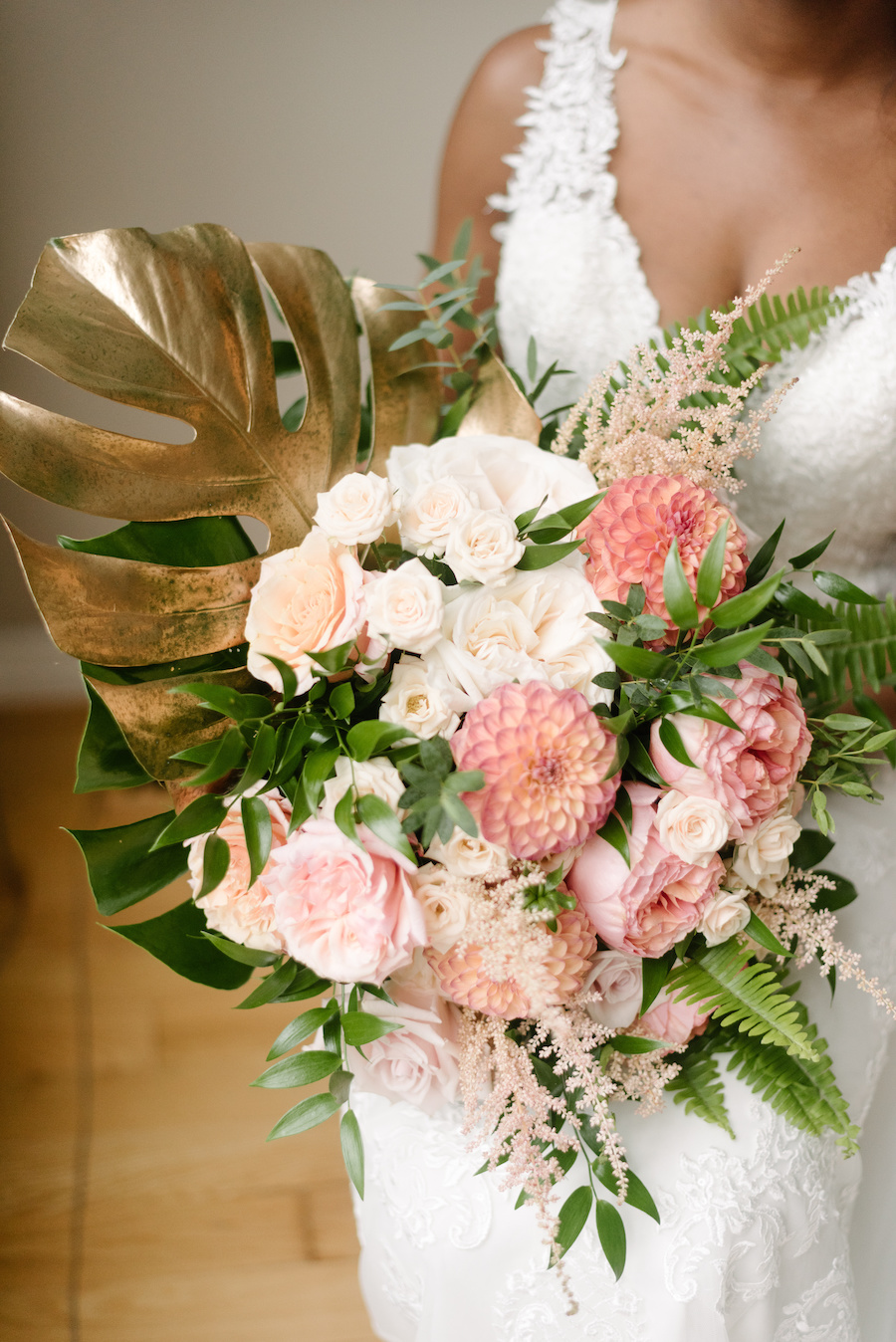 Photo of a bride holding a summer bouquet of tropical flowers, ferns and monstera leaves