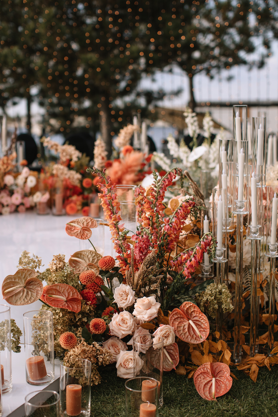 Photo of an arrangement of orange tropical flowers surrounded by orange candles at an event.