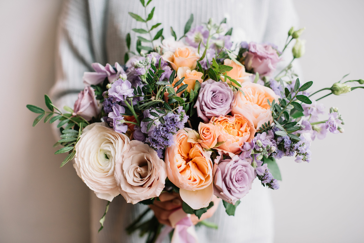 A person holding a bouquet of pastel-colored flowers.