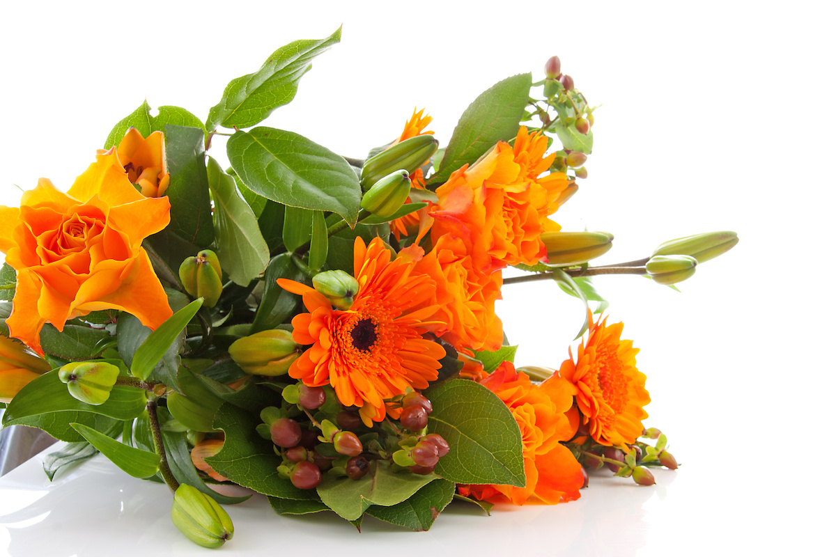 A warm-toned bouquet of flowers and foliage featuring orange flowers and leafy greens.