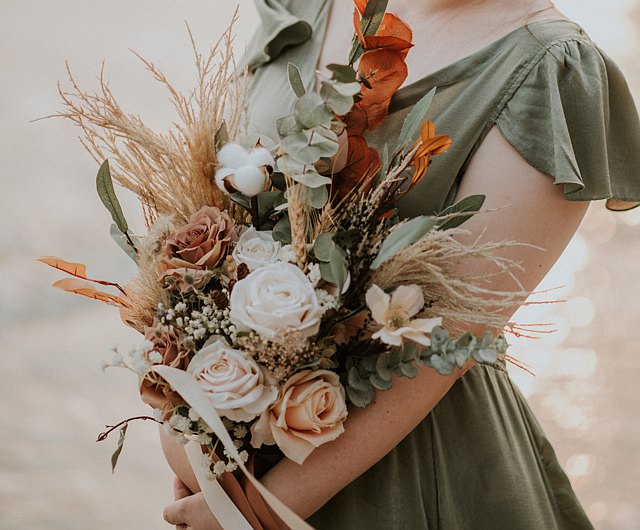 A woman in a green dress holding a bouquet of earth-toned flowers.