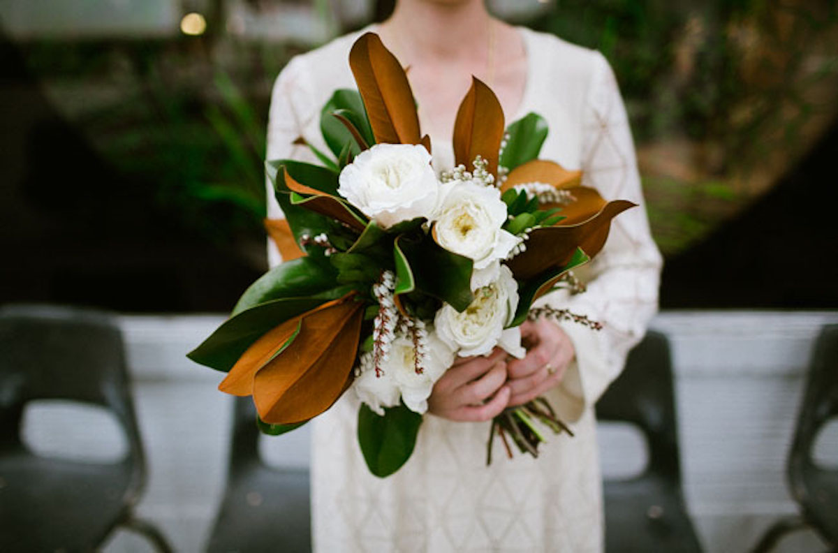 A woman holding a bouquet of white flowers with filler foliage around them.