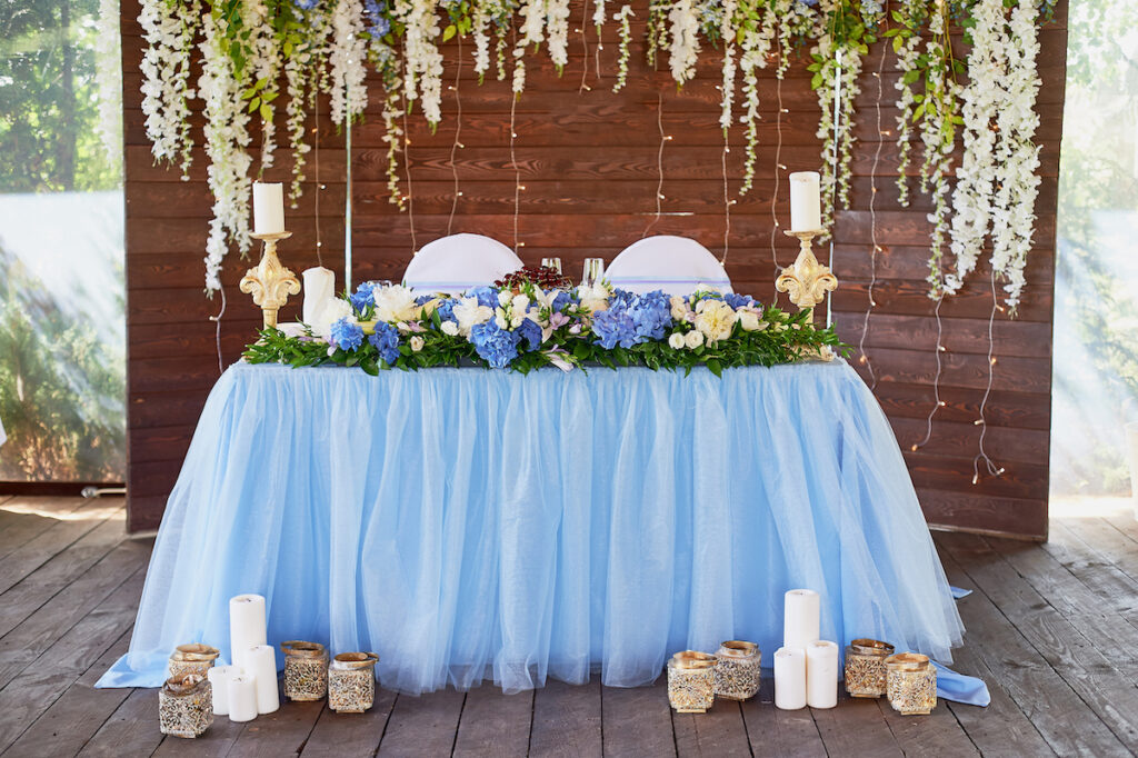 A table with a blue tablecloth and hanging foliage coming from above it.