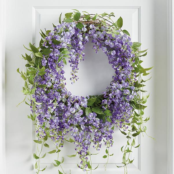 A wreath hanging on a door with purple flowers and green hanging foliage.