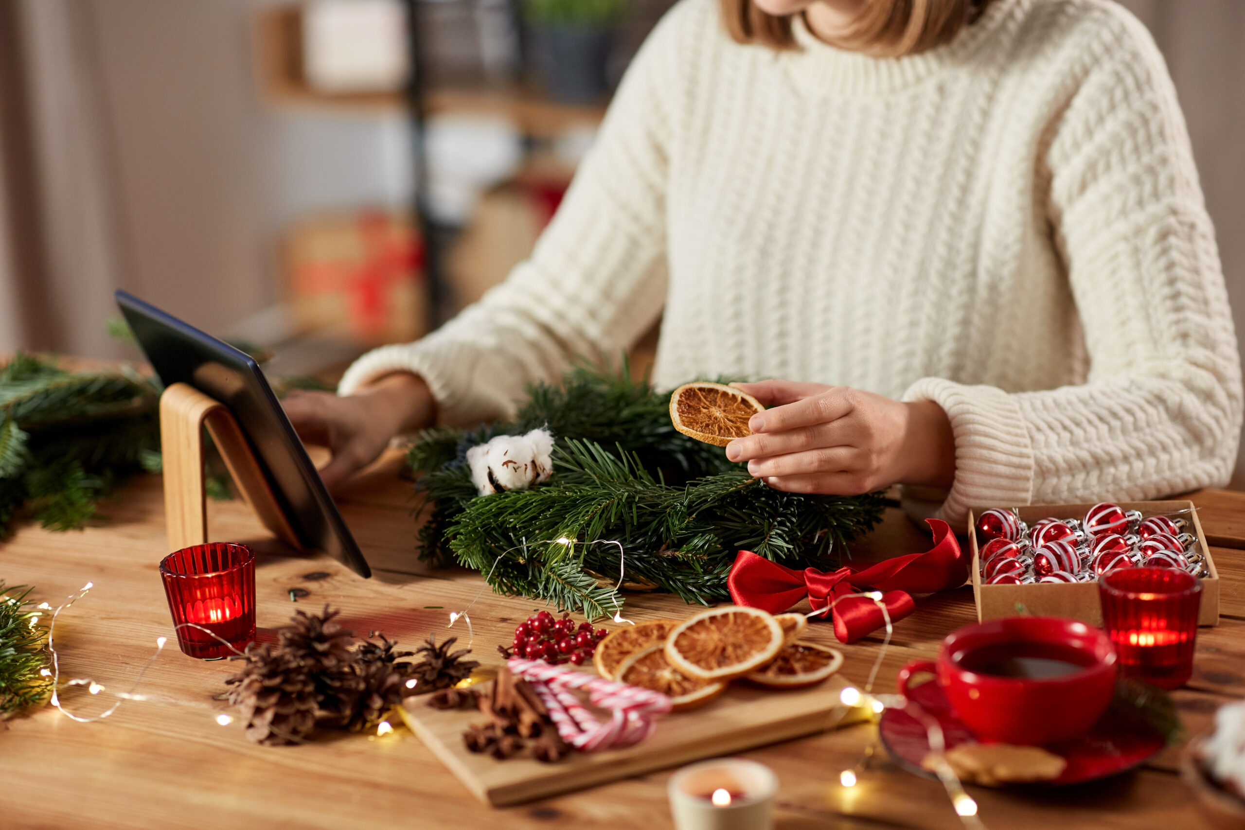 A person decorating a cedar garland with dried orange slices and cinnamon sticks.