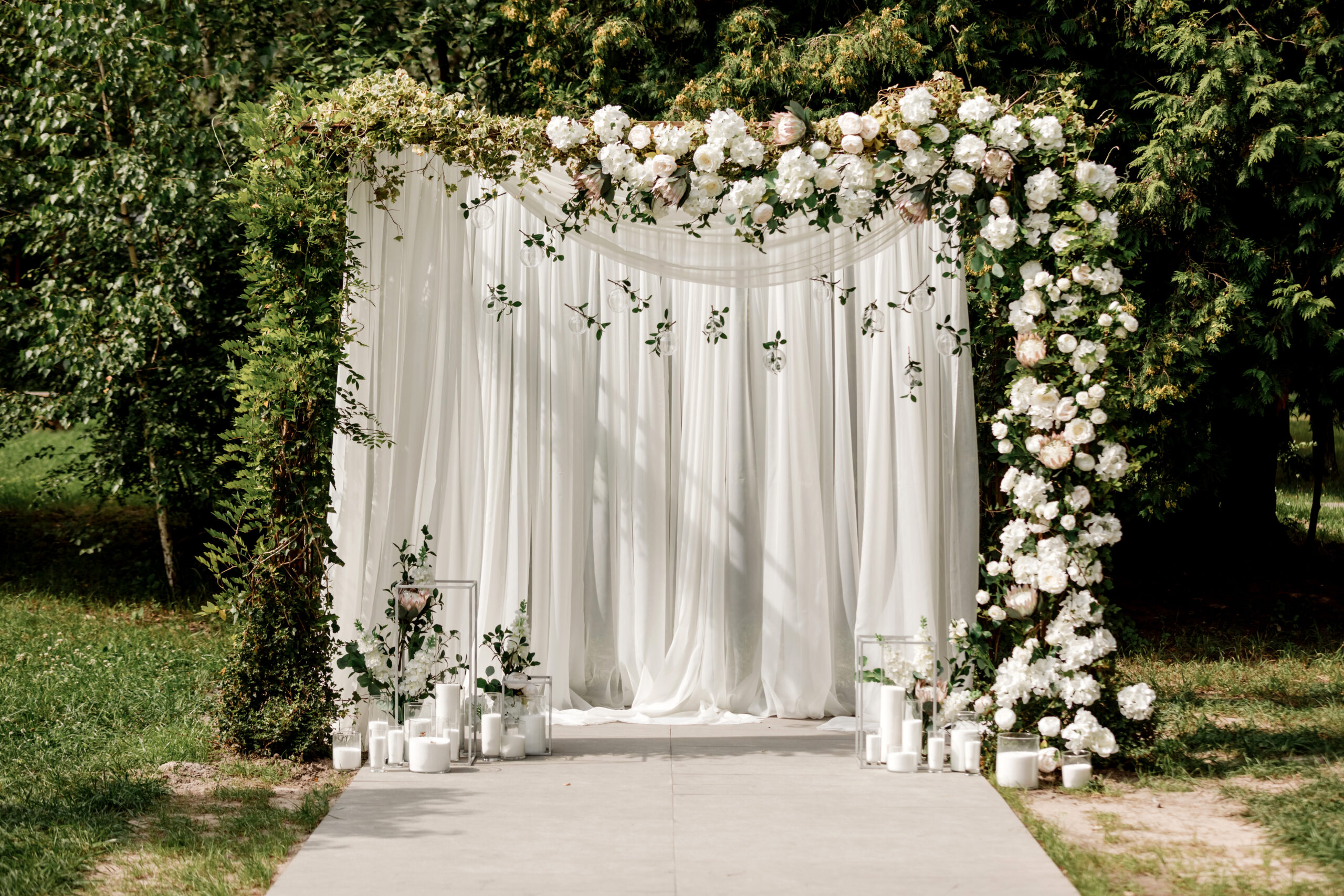 An outdoor wedding arch elegantly draped in white fabric and adorned with white flowers and greenery.