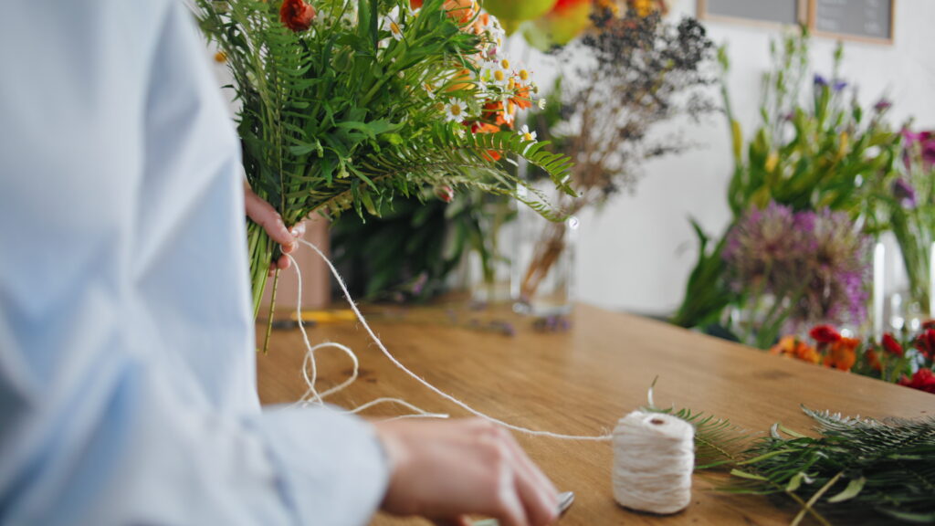 A florist tying a string around a vibrant bouquet with a variety of flowers, including bright ferns.