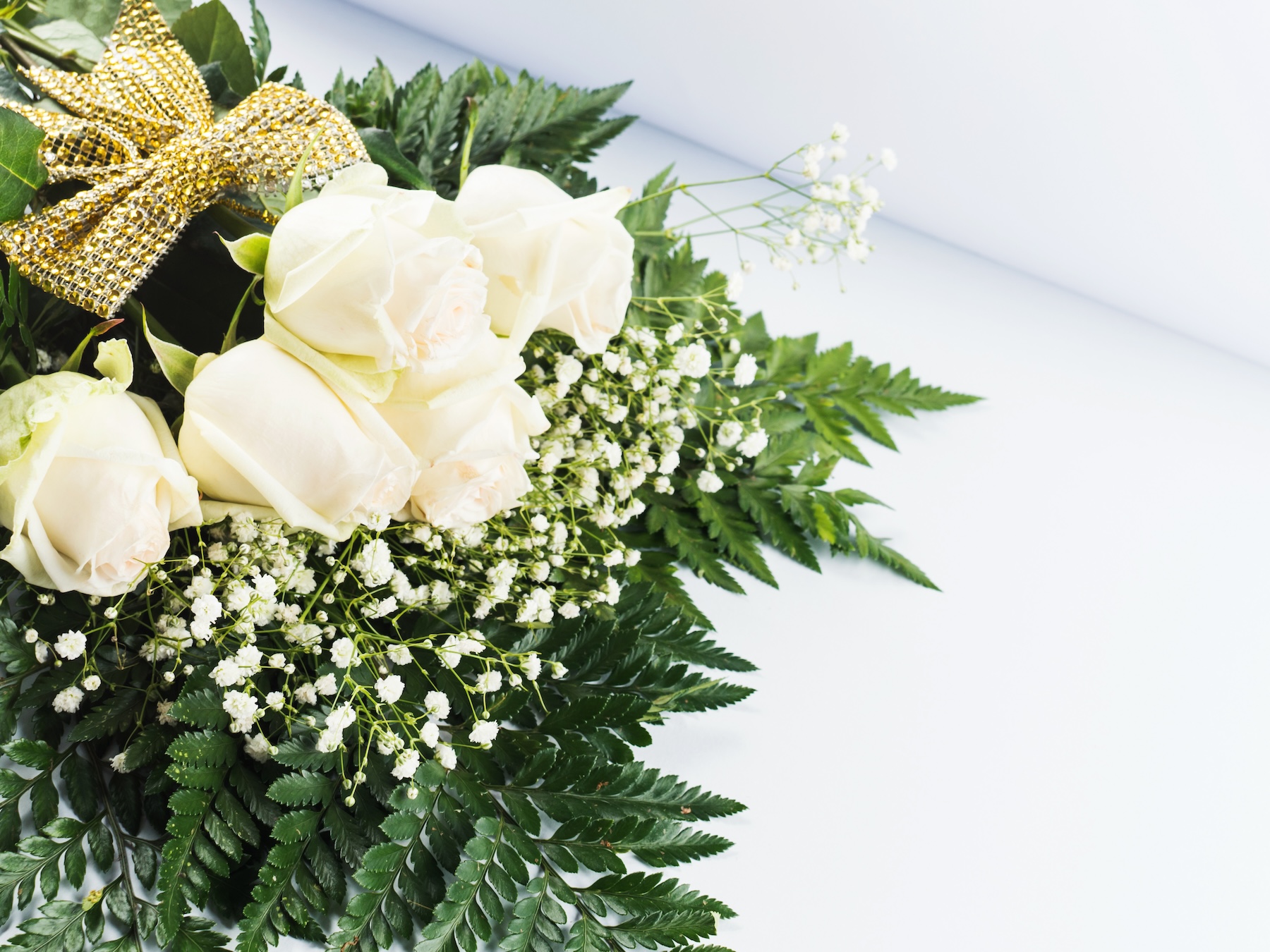 An elegant Mother's Day arrangement of pale roses and baby's breath with ferns, adorned with a golden bow.
