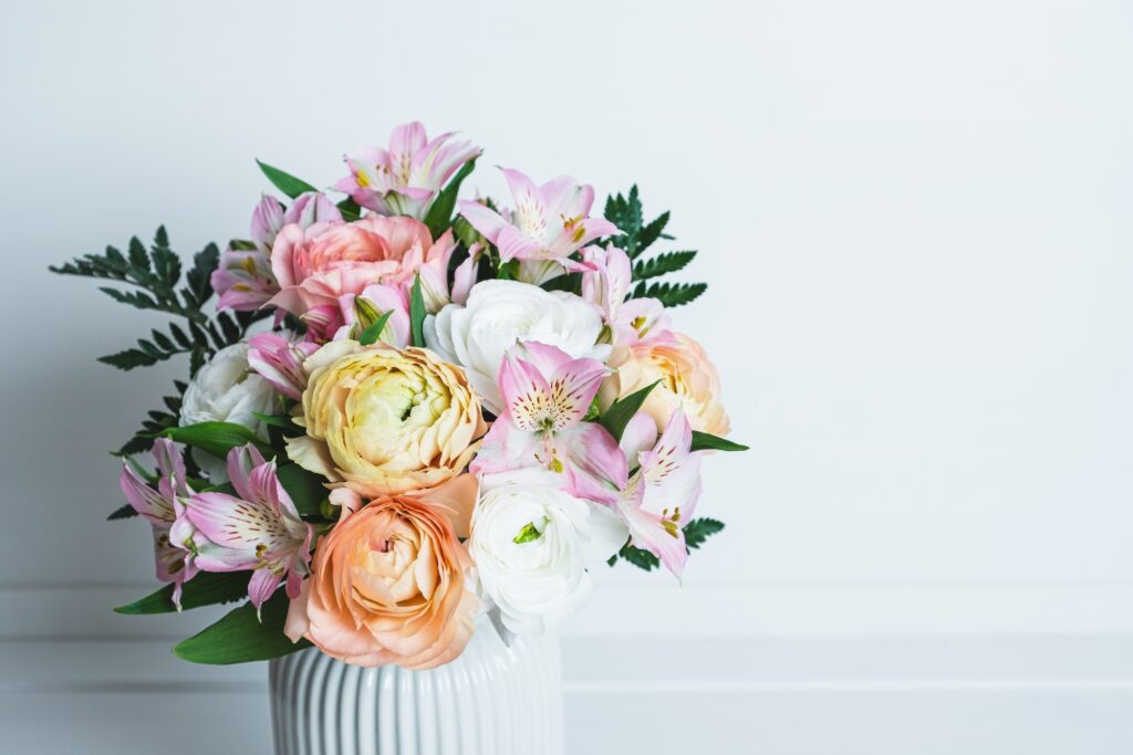 A white vase containing a Mother's Day arrangement of pastel flowers and ferns.